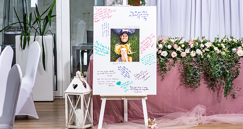 Une grande toile photo avec une photo de couple amoureux, autour des vœux écrits par des invités de mariage. A côté une lanterne blanche, au fond une table décorée de tulle rose et de fleurs.